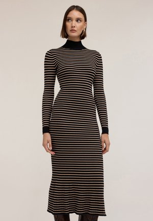 Sukienka z prążkowanego materiału w poziome paski, z długimi rękawami, wysokim dekoltem i rozszerzanym dołem. Kolory to czarne i beżowe paski.
