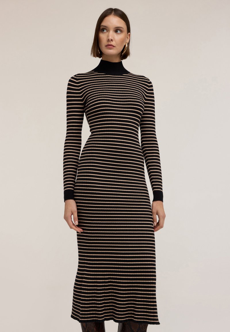 Sukienka z prążkowanego materiału w poziome paski, z długimi rękawami, wysokim dekoltem i rozszerzanym dołem. Kolory to czarne i beżowe paski.