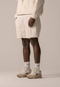 Light beige athletic apparel featuring a zip-up top and matching shorts. Sneakers are beige with black accents and thick white socks.