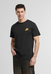 Svart bomulls t-skjorte med en liten, fargerik pizzagrafikk brodert på øvre venstre bryst. Klassisk rund halslinning og korte ermer.