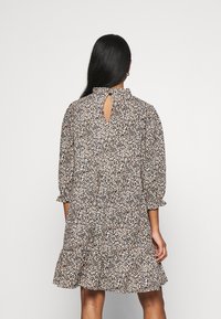 Kleid mit Blumenmuster, 3/4-Ärmeln, Schlitz im Rücken und Rüschensaum. Die Farben umfassen Schwarz, Weiß sowie verschiedene Schattierungen von Orange und Beige.