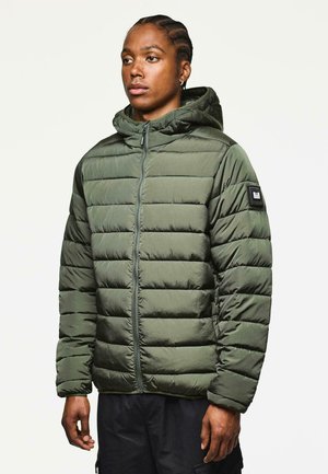 Chaqueta acolchada verde oscuro con capucha, cierre de cremallera en la parte delantera, diseño acolchado y un parche en la manga izquierda. Textura suave con un acabado mate.