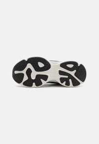 Black and white sneaker outsole with a textured rubber surface, featuring a distinctive tread pattern and flexible grooves for grip.