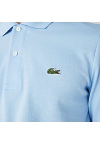 Lyseblå polo-shirt i struktureret bomuld med en to-knaps placket og et grønt krokodille-logo broderet på venstre bryst.