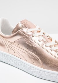 Metallisk roséguld sneaker med vita snören och texturerad vit sula. Har subtil branding och slät ovandel med perforerade detaljer.