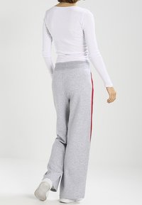 Grå sweatpants med avslappnad passform, med röd sidremsa, elastisk midja och mjuk tygtextur. Vit långärmad topp synlig.