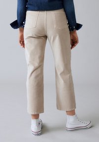 Pantalones recortados beige con bolsillos traseros, combinados con zapatillas altas blancas. La tela parece suave, con una textura lisa y un ajuste estructurado.