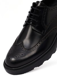 Zwarte leren nette schoen met een wingtips ontwerp, geperforeerde details en zwarte veters. Beschikt over een ronde neus en een gestructureerde zwarte rubberen zool.