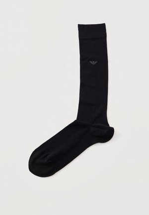 Une chaussette noire mi-mollet avec un petit logo gris, présentée sur un fond blanc.