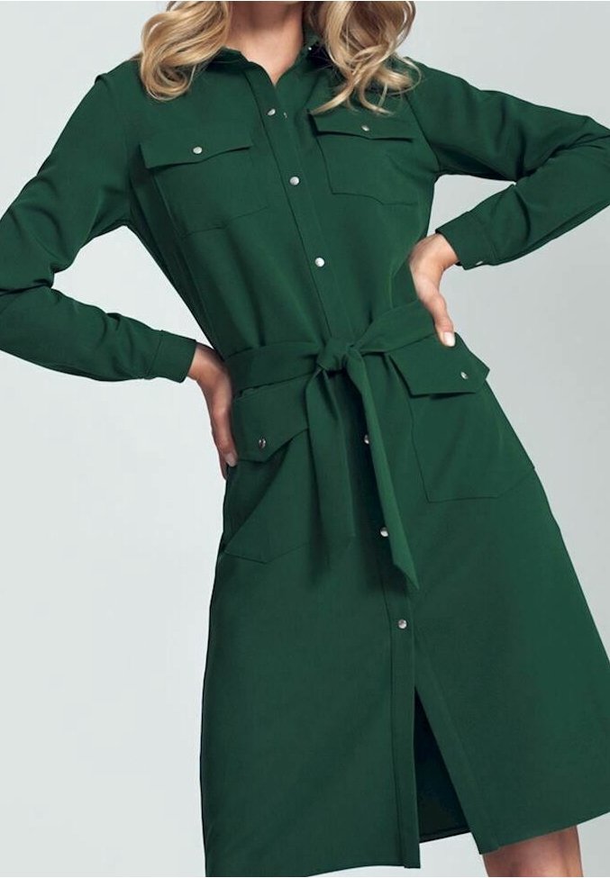 Femme portant une robe vert foncé à manches longues, boutonnée, avec des poches à rabat à l'avant et une ceinture nouée à la taille, posant avec les mains sur les hanches.
