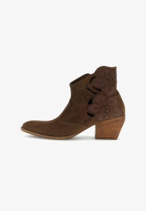 Bruine suède enkellaars met lage gestapelde hak en uitgesneden bloemenleren applicaties aan de buitenkant.