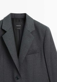Grå uld blazer med spids lapel, en enkelt knaplukning og en venstre brystlomme. Mærke synligt indeni. Glat tekstur, skræddersyet design.