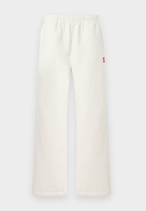 Laiad-tallaga beežid püksid, millel on elastne vöökoht ja väike punane plaastrikoht paremal küljel, seisavad tavalise heleda tausta ees.