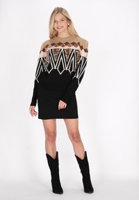 Fustă mini neagră asociată cu un pulover cu un model de zigzag în tonuri de bej, maro și negru, decorat cu mărgele. Modelul poartă cizme până la genunchi.