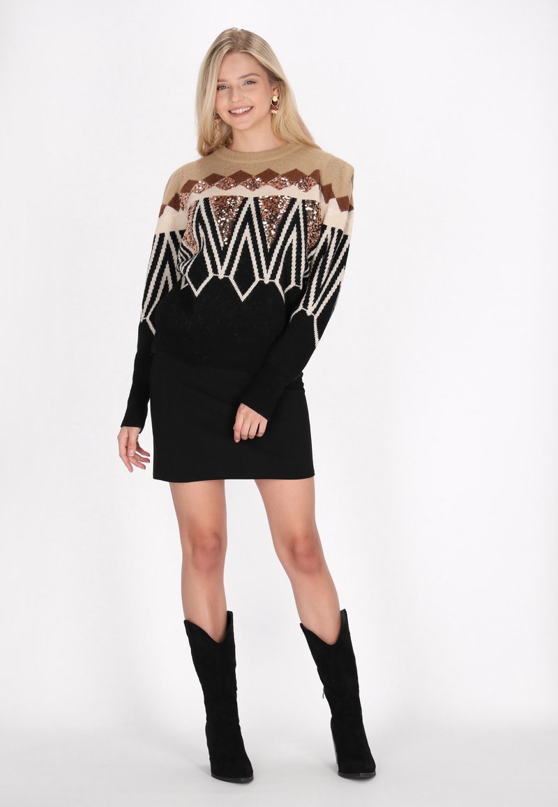 Fustă mini neagră asociată cu un pulover cu un model de zigzag în tonuri de bej, maro și negru, decorat cu mărgele. Modelul poartă cizme până la genunchi.