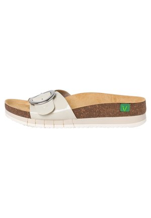 Slide sandal with a glossy cream upper, large silver buckle detail, cork midsole, and white rubber outsole with textured tread. Green logo accent.