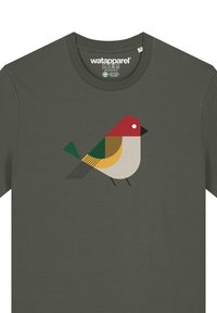 T-shirt vert olive avec un graphique stylisé d'oiseau en rouge, jaune, vert et beige, accompagné de formes géométriques et d'accents noirs.