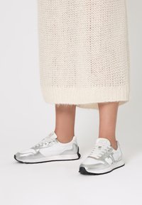 Sneaker sportive argentate con una combinazione di texture lisce e metallizzate, caratterizzate da una tomaia in rete bianca e una suola in gomma nera.