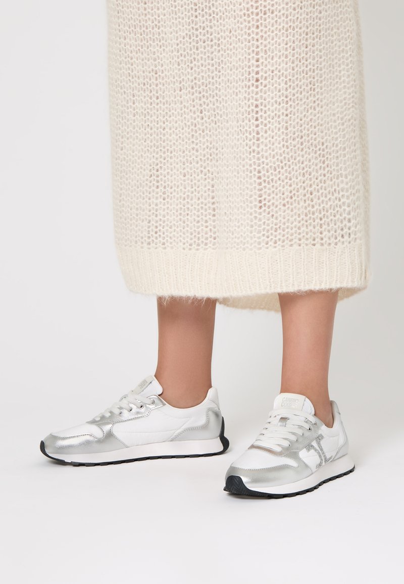 Sneaker sportive argentate con una combinazione di texture lisce e metallizzate, caratterizzate da una tomaia in rete bianca e una suola in gomma nera.