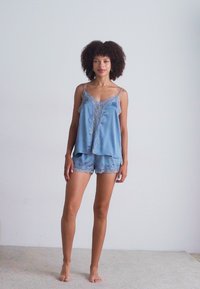 Light blue satin pajama set featuring a lace-trimmed camisole top and matching shorts, with adjustable straps and a relaxed fit.