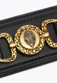 Czarny skórzany pasek z okrągłą złotą klamrą, która ma wygrawerowane pióra i otoczona małymi złotymi ćwiekami.