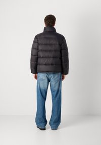 Padded black puffer jacket with a high collar, featuring horizontal quilting. Worn with light blue wide-leg jeans, viewed from the back.