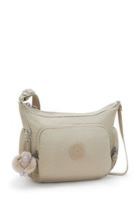 Beżowa torba crossbody wykonana z teksturowanej tkaniny, z przednią kieszonką, okrągłym logo i przyczepioną puszystą breloczkiem w kształcie małpki.