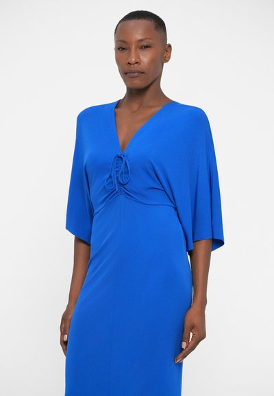 Modra obleka z globokim V-izrezom in drapanimi rokavi, ki ima zbrano lepo podrobnost na pasu. Gladek, lahki material v enotni barvi.