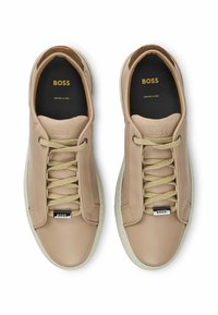 Beige leather sneakers with beige laces, branded detailing on the tongue, and a contrasting white rubber sole, featuring a smooth texture.
