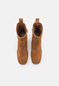 Bottes bottines en daim beige à finition lisse, dotées d'une fermeture éclair latérale et d'une languette pour un enfilage facile. Design minimaliste et bout arrondi.