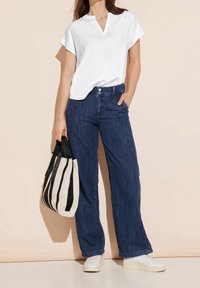 Blusa bianca a maniche corte con scollatura a V, abbinata a jeans in denim blu a gamba larga. Una borsa a tracolla a righe bianche e nere completa il look.