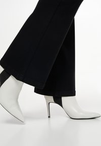 Witte enkellaarsjes met een spitse neus en stilettohak, met een zwart zijpaneel. Gecombineerd met donkerdenim flared pants.