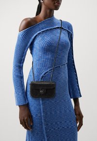 Abito a maglia blu a coste con design off-shoulder, caratterizzato da dettagli con bottoni; borsa nera testurizzata con catena e dettaglio logo.