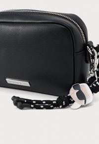 Černá kožená taštička se stříbrným zipem, zdobená černo-bílým spleteným popruhem a hravým přívěskem.