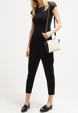 Woman wearing black lace cap sleeve top and high-waist black cropped pants, carrying black and white shoulder bag with black loafers.