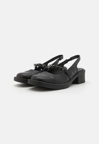 Pantofi slingback din piele neagră cu toc mediu. Au o curea decorativă cu ținte metalice. Textură netedă și design cu vârf rotund.