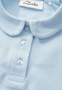 Svetlomodrá polo košeľa s textúrovanou látkou, s golierom a tromi gombíkmi v tvare srdca na légii, označená značkou Clarks.