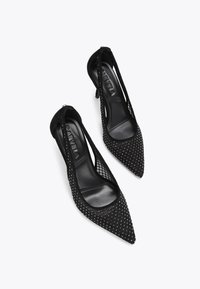 Des chaussures à talons hauts noires avec un embout pointu, présentant un design en maille, des clous décoratifs et un intérieur en cuir lisse.