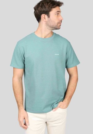 T-shirt texturé turquoise à manches courtes et col rond. Comprend un logo imprimé subtil en blanc sur la poitrine. Associé à un pantalon de couleur claire.