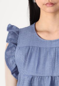 Top azzurro chiaro con maniche arricciate realizzato in tessuto testurizzato. Presenta un collo rotondo e un design del corpo arricciato e fluido.
