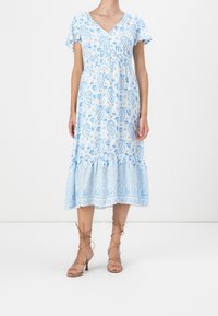 Robe bleue clair à motif paisley avec des manches flutter courtes, un décolleté en V et un ourlet en volants à étages. Fabriquée en tissu respirant, sandales à enrouler autour de la cheville.