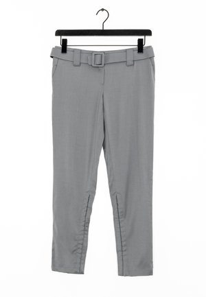 Pantaloni grigi su misura con cintura, dotati di tasche e zip alla caviglia, realizzati in tessuto liscio e appesi a un gancio nero.