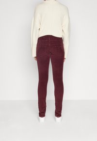 Burgundowe skinny jeans z weluru o miękkiej fakturze, wysoki stan, z tylnymi kieszeniami, połączone z kremowym, oversize'owym swetrem i białymi sneakersami.