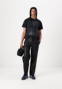 Black graphic t-shirt with a geometric print, paired with black wide-leg trousers and blue sneakers with white stripes. Small black bag included.