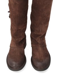 Hnědé semišové kozačky ke kolenům s kulatou špičkou, plochou podrážkou a viditelným šitím. Na boku mají dekorativní kovové doplňky.