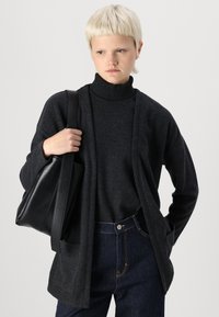 Svart läderhandväska, mörkgrå tröja och cardigan i avslappnad passform. Anmärkningsvärd ribbad krage och texturerad tyg. Mörk denimjeans med sömmar.
