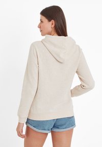 Beige hoodie with a drawstring hood, long sleeves, and ribbed cuffs. Worn with rolled denim shorts, showing a relaxed, casual fit.