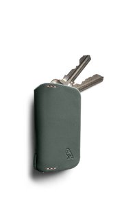 Porte-clés en cuir vert avec des bords arrondis, présentant une couture en cuivre et un logo de hibou en relief. Deux clés dépassent du dessus.