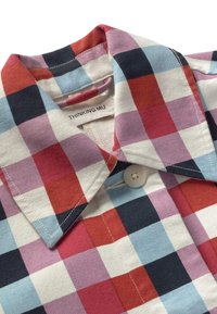 Gros plan sur le col d'une chemise à carreaux multicolore avec des carrés rouges, bleus, marine, violets et blancs et un bouton blanc.