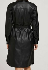 Schwarzes Lederkleid mit langen Ärmeln, tailliertem Gürtel und glatter Textur. Verfügt über einen geraden Schnitt mit Nahtdetails auf der Rückseite.